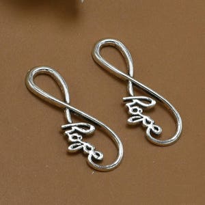Puede incluir: Dos encantos de plata en forma de símbolo de infinito con la palabra "Love" inscrita dentro de cada lazo.