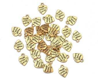 May include: A pile of gold-colored metal heart-shaped charms with the words "Made with Love" and "Love with Arrow" printed on them.