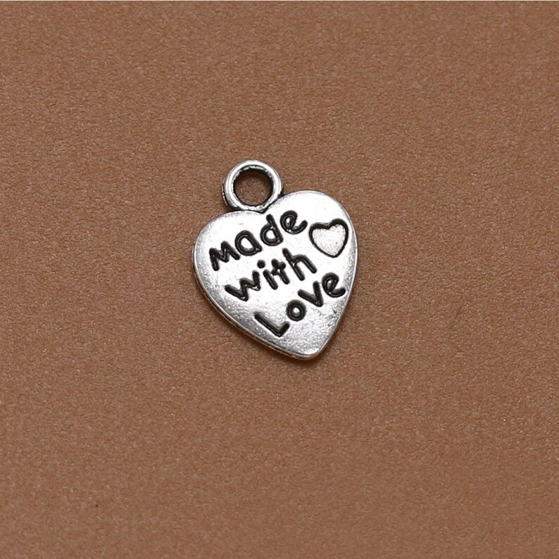 May include: Silver heart-shaped charm with the words "Made with Love" and a small heart.