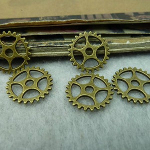 May include: Five antique gold-toned metal gears with a decorative design. The gears are arranged in a semi-circle on a white surface.