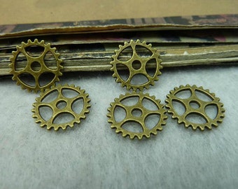 Puede incluir: Cinco engranajes de metal de color dorado antiguo con un diseño decorativo. Los engranajes están dispuestos en semicírculo sobre una superficie blanca.