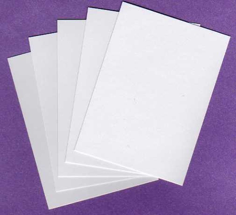 May include: A stack of five white rectangular papers fanned out against a purple background. The papers are clean and crisp, with a smooth surface. The arrangement suggests a presentation or stationery item.