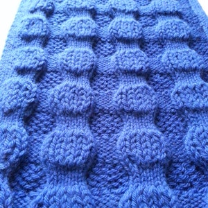 May include: A close-up of a blue knitted fabric with a textured pattern of raised circles.