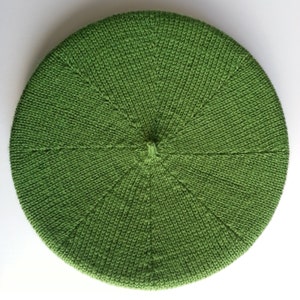 Peut inclure: Un béret en tricot vert avec une forme circulaire et une surface texturée.