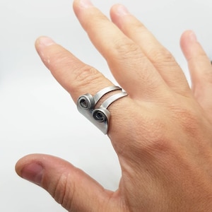 Può includere: Un anello d'argento con un design unico che presenta due bande curve sovrapposte e due accenti circolari.