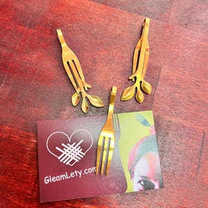 May include: Three gold-toned metal fork-shaped bookmarks with leaf designs. The bookmarks are on a burgundy card with the text "GlemLety.com".