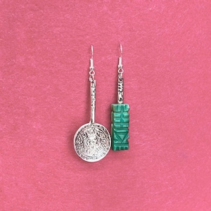 May include: A pair of silver earrings with green stone accents. One earring features a circular design with intricate details, while the other has a rectangular shape with a carved design.