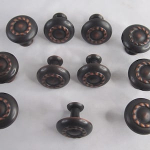 May include: Twelve bronze cabinet knobs with a rope design around the edge. The knobs have a copper finish.