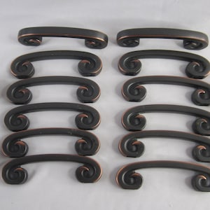 May include: A set of 12 black cabinet pulls with a copper finish. The pulls have a decorative scroll design.