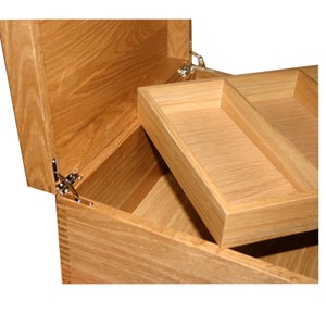 May include: A light brown wooden box with an open lid and a removable interior tray featuring two compartments. The box is constructed with visible finger joints at the corners and includes metal hinges that secure the lid to the main body.