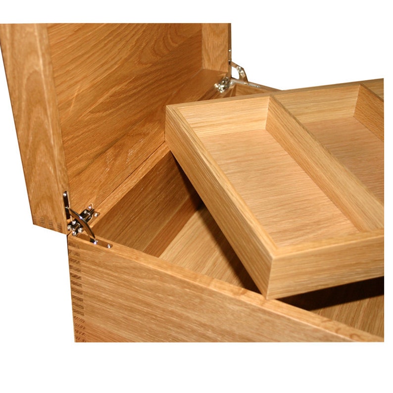 May include: A light brown wooden box with an open lid and a removable interior tray featuring two compartments. The box is constructed with visible finger joints at the corners and includes metal hinges that secure the lid to the main body.