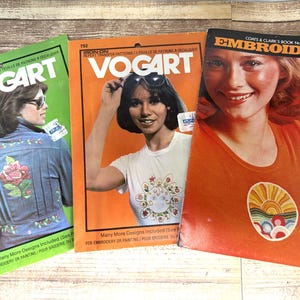 May include: Three vintage Vogart embroidery pattern books. The covers feature women and colorful designs. One book is green, one is orange, and the third is orange with the word "Embroidery" on it.