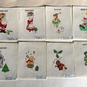 May include: Eight rectangular fabric panels featuring embroidered Christmas stocking outlines and holiday characters including Santa, a child, an elf, a mouse, a rabbit, a figure with a staff, a bee, and a snowman, each labeled with SOLD OUT text.