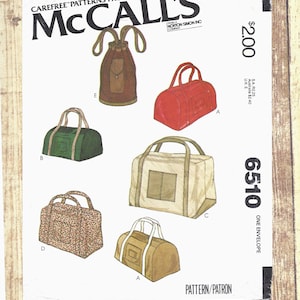 May include: A McCall's 6510 sewing pattern envelope featuring illustrations of various bags. The designs include a brown drawstring backpack, a red duffel, a green duffel, a large beige rectangular bag, a floral print duffel, and a tan duffel bag.