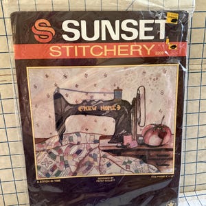 May include: A Sunset Stitchery needlepoint kit titled A Stitch In Time, designed by Patsy Gullett. The package features an illustration of a vintage New Home sewing machine, a quilt, and a tomato pincushion. It is designed to fit an 8 inch by 10 inch frame.