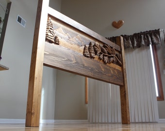 May include: A wooden headboard with a carved mountain and pine tree design. The headboard is made of natural wood with a dark brown stain.