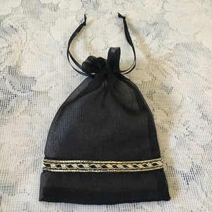 K&ouml;nnte beinhalten: Eine schwarze Kordeltasche mit goldener Einfassung. Die Tasche ist aus einem durchsichtigen Stoff gefertigt und hat einen Kordelverschluss.