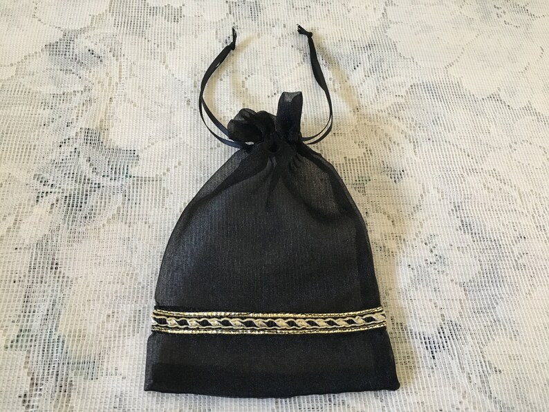 K&ouml;nnte beinhalten: Eine schwarze Kordeltasche mit goldener Einfassung. Die Tasche ist aus einem durchsichtigen Stoff gefertigt und hat einen Kordelverschluss.