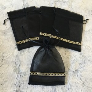 K&ouml;nnte beinhalten: Satz mit sechs schwarzen Organza-Geschenkt&uuml;ten mit goldener Verzierung. Die Taschen sind aus durchsichtigem Stoff und haben einen Kordelverschluss.