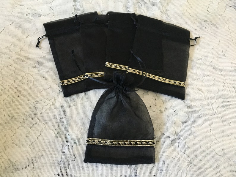 K&ouml;nnte beinhalten: Satz mit sechs schwarzen Organza-Geschenkt&uuml;ten mit goldener Verzierung. Die Taschen sind aus durchsichtigem Stoff und haben einen Kordelverschluss.