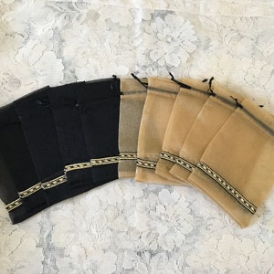 K&ouml;nnte beinhalten: Ein Set mit 14 kleinen, durchsichtigen Beuteln mit Kordelzug. Die H&auml;lfte der Beutel ist schwarz und die andere H&auml;lfte beige. Jeder Beutel hat einen schwarzen und goldenen Besatz am oberen Rand.