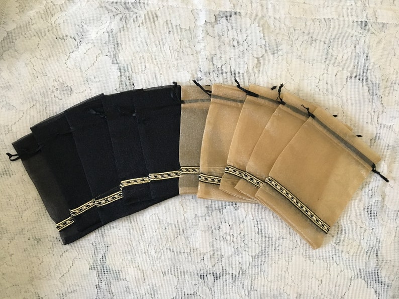 K&ouml;nnte beinhalten: Ein Set mit 14 kleinen, durchsichtigen Beuteln mit Kordelzug. Die H&auml;lfte der Beutel ist schwarz und die andere H&auml;lfte beige. Jeder Beutel hat einen schwarzen und goldenen Besatz am oberen Rand.