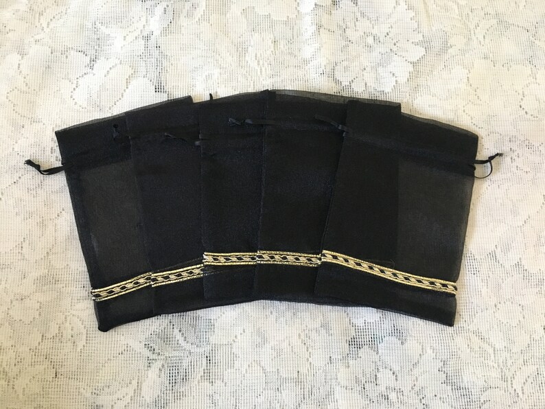 K&ouml;nnte beinhalten: Sechs schwarze Organza-Geschenkbeutel mit goldener Einfassung. Die Beutel sind in einer Reihe angeordnet und haben einen Kordelverschluss.