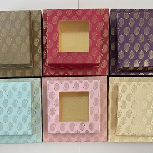 May include: An assortment of decorative gift boxes in various colors, including gold, red, purple, light blue, pink, and beige. Each box features a paisley pattern and a matching lid. Some boxes have a square window.