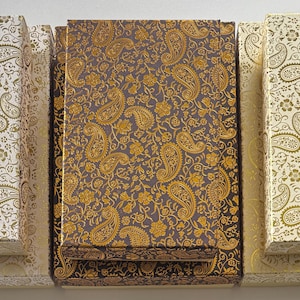 May include: An overhead shot of several rectangular boxes with lids. The boxes are decorated with a paisley pattern in gold and cream, and gold and dark brown. The boxes are arranged in a row.