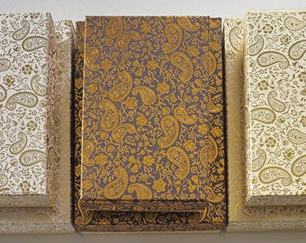 May include: An overhead shot of several rectangular boxes with lids. The boxes are decorated with a paisley pattern in gold and cream, and gold and dark brown. The boxes are arranged in a row.