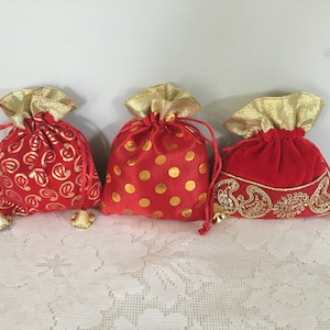 May include: Three red drawstring pouches with gold accents. The pouches have different patterns: paisley, polka dots, and embroidered designs. Each pouch has a gold-colored drawstring and a small bell charm.