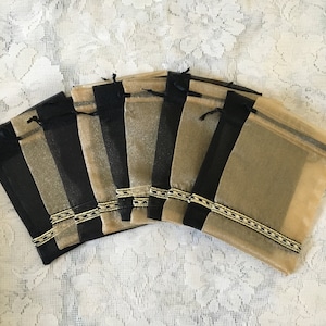 K&ouml;nnte beinhalten: Ein Set aus acht kleinen, durchsichtigen, goldenen und schwarzen Beuteln mit Kordelzug. Die Beutel haben einen goldenen und schwarzen Besatz am oberen Rand.