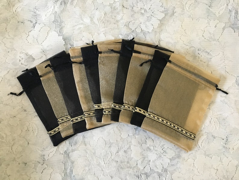 K&ouml;nnte beinhalten: Ein Set aus acht kleinen, durchsichtigen, goldenen und schwarzen Beuteln mit Kordelzug. Die Beutel haben einen goldenen und schwarzen Besatz am oberen Rand.