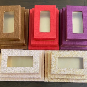 May include: Five decorative boxes with clear windows. The boxes are stacked in pairs. The top boxes are brown, red, and purple. The bottom boxes are beige with a white floral pattern.