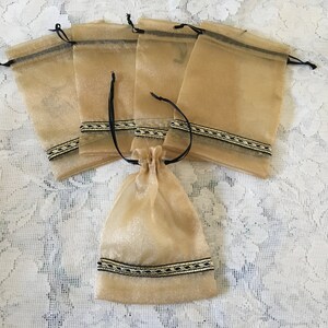 K&ouml;nnte beinhalten: Satz mit sechs kleinen, durchsichtigen, goldfarbenen Beuteln mit schwarzem und goldenem Besatz. Die Beutel sind aus einem zarten, durchscheinenden Stoff gefertigt und haben einen gerafften oberen Rand.