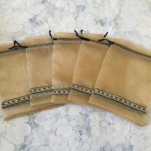 K&ouml;nnte beinhalten: Sechs kleine, beigefarbene Organza-Geschenkbeutel mit schwarzem und goldenem Besatz. Die Beutel haben Kordelz&uuml;ge und sind perfekt f&uuml;r kleine Geschenke oder Mitbringsel.
