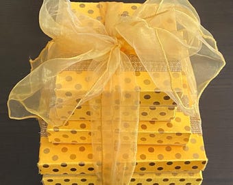 May include: A stack of four yellow gift boxes with black polka dots, tied together with a yellow sheer ribbon.
