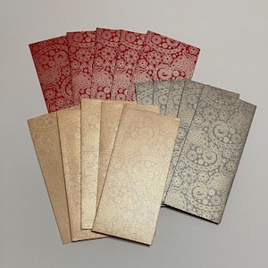 May include: A stack of red and gold patterned envelopes, and a stack of gray and gold patterned envelopes.