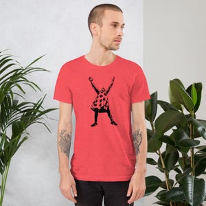 Może przedstawiać: Czerwony t-shirt z czarną sylwetką osoby w kropkowanej sukience, podnoszącej ręce w górę.