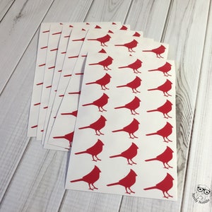 May include: A stack of white sheets with red cardinal silhouettes printed on them. The sheets are stacked on a light wood surface.