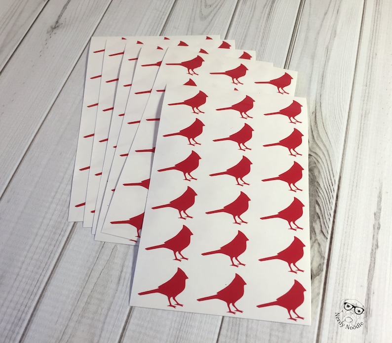 May include: A stack of white sheets with red cardinal silhouettes printed on them. The sheets are stacked on a light wood surface.