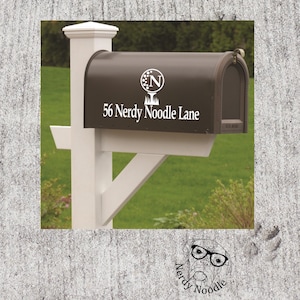 May include: A brown mailbox with a white vinyl sticker that says "56 Nerdy Noodle Lane" and a white circle with the letter "N" inside. The mailbox is mounted on a white post.