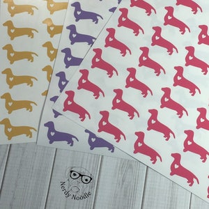K&ouml;nnte beinhalten: Drei Bl&auml;tter Stickerpapier mit Dackel-Silhouetten. Die Sticker sind in Pink, Lila und Gelb. Jeder Dackel hat ein kleines Herz auf der Brust.