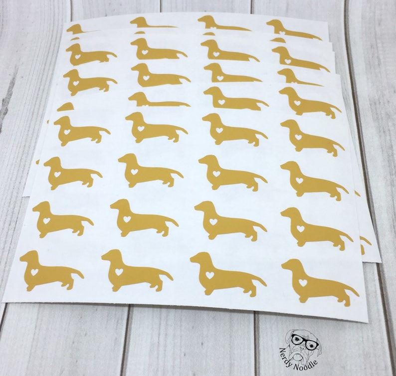K&ouml;nnte beinhalten: Ein Blatt wei&szlig;es Papier mit mehreren goldenen Dackel-Aufklebern. Jeder Dackel hat ein kleines wei&szlig;es Herz auf der Brust.