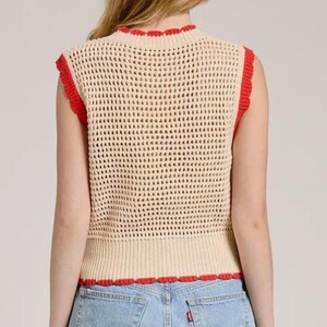 K&ouml;nnte beinhalten: Eine &auml;rmellose H&auml;kelweste in hellem Beige mit einem strukturierten Netzmuster. Das Kleidungsst&uuml;ck ist mit einem leuchtend roten, wellenf&ouml;rmigen Saum am Rundhalsausschnitt, an den Armausschnitten und am geraden unteren Abschluss an der Taille versehen.