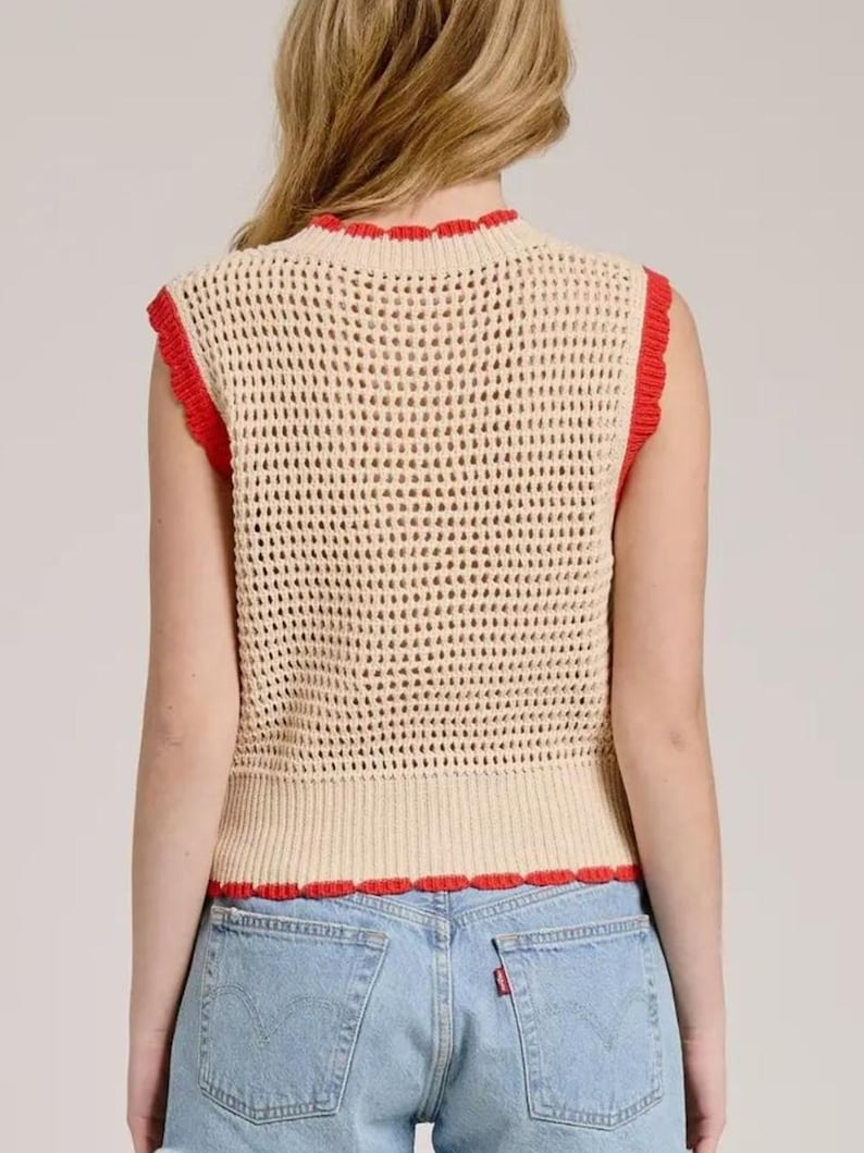 K&ouml;nnte beinhalten: Eine &auml;rmellose H&auml;kelweste in hellem Beige mit einem strukturierten Netzmuster. Das Kleidungsst&uuml;ck ist mit einem leuchtend roten, wellenf&ouml;rmigen Saum am Rundhalsausschnitt, an den Armausschnitten und am geraden unteren Abschluss an der Taille versehen.