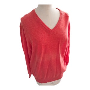 May include: A coral V-neck sweater. The long-sleeved sweater is displayed on a mannequin. The sweater has a ribbed hem and cuffs. The neckline is a deep V-shape.