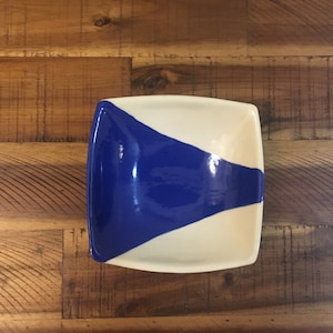 Puede incluir: Un plato cuadrado de cerámica con un esmalte blanco y un diseño de esmalte azul. El esmalte azul tiene la forma de un triángulo.