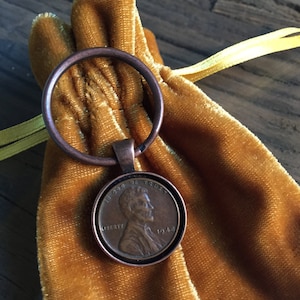 May include: A 1948 US penny coin on a gold velvet pouch with a copper ring attached.