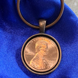 May include: A copper penny keychain with a 1992 penny encased in a clear resin. The penny features the profile of Abraham Lincoln and the inscription "In God We Trust" and "Liberty".